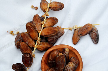 Dates (Phoenix dactylifera) on a wooden bowl on a white cloth background. food for breaking the fast during Ramadan for Muslims. selective focus