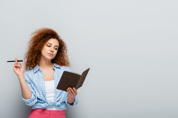 thoughtful woman in plaid shirt holding pen and notebook on grey background