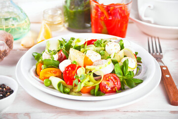 salad of fresh cherry tomatoes, mozzarella, basil, radish and other greens on the dinner table