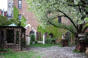 New York City - April 18 2021: Red brick building covered in ivy with ornamental columns and figures in Elizabeth Street Garden in Nolita, Manhattan.