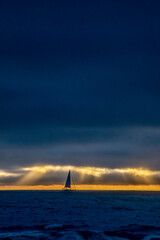 The silhouette of a sailboat is set against a colorful sunset and storm clouds on the Pacific Ocean off the coast of California.