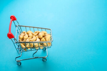 Food cart filled with peeled cashews on a blue background. Copy space.