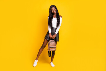 Full length body size photo black skinned brunette smiling holding rucksack wearing short skirt isolated on vibrant yellow color background