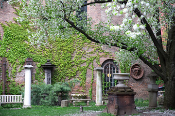 New York City - April 18 2021: Red brick building covered in ivy with ornamental columns and figures in Elizabeth Street Garden in Nolita, Manhattan.