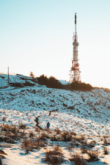 Two guys hiking on a snowy hill with a big radio antenna on the top during sunset