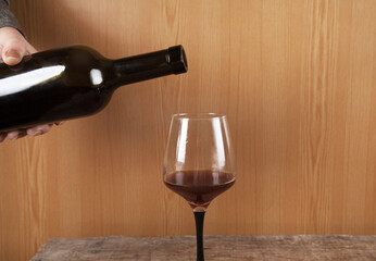 Wine pouring in glass, wooden background.