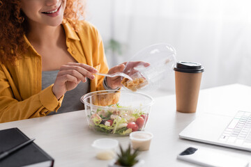 partial view of smiling teleworker holding plastic fork near fresh salad and takeaway drink