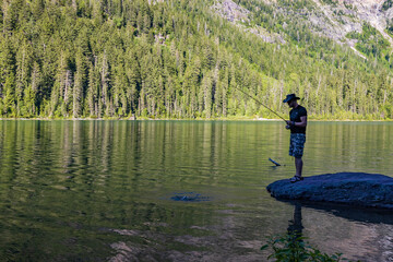 Fototapeta na wymiar Fisherman at Avalanche Lake and surrounding mountain range at Glacier National Park
