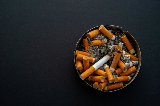Close up many cigarette butts in full and dirty  ashtray isolated on black background copy space for text design