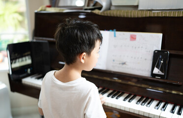 A boy is studying piano online with tablet.