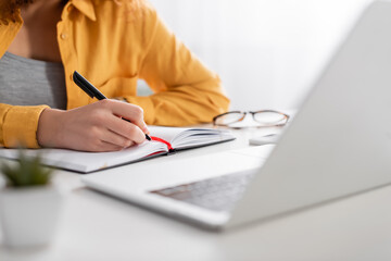 cropped view of freelancer writing in notebook near laptop on blurred foreground