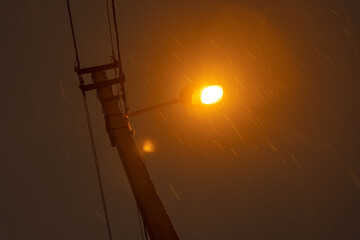 Old orange street light with electricity wires, long exposure during snowfall / rain at night.