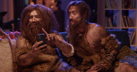 Wild bearded man in animal savage fur taking selfie picture on smartphone camera interacting...