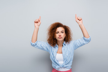 serious woman pointing up with fingers while looking at camera on grey background