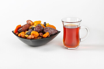 A cup of tea and a mixture of dried fruits in a plate on a white background.