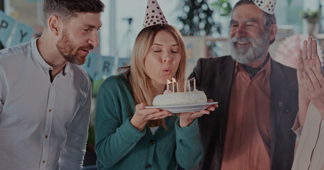 Excited caucasian blonde woman mother gathering her family around, holding cake and blowing candles making birthday wish celebrating together. Home interiors.