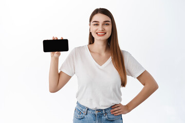 Technology. Smiling beautiful woman shows phone horizontal screen, looking pleased, recommending website, online shopping store or application, standing over white background