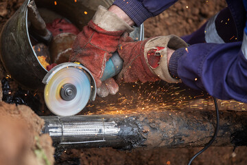 a man in working form is working on production, factory physical labor, a man is holding a Bulgarian, he is sawing an iron pipe with a metal disk, sparks are flying, dangerous work
