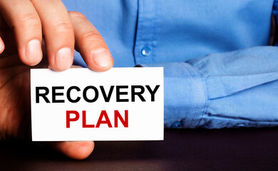 RECOVERY PLAN is written on a white business card in a man's hand. Advertising concept