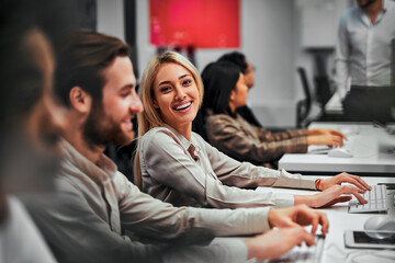 Young adult business people working on computers with colleagues in a spacious office. Data...