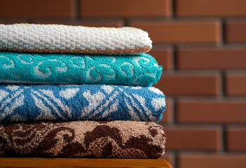 Stack of clean bath towels on wooden table near red brick wall