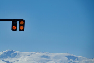 Climate change concept: Caution light sign with snowy mountains in the background