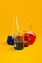 Flat bottom flask, conical flask and two Berzelius beaker glasses lay against mustard yellow background