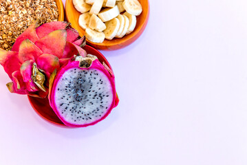Plate with sliced ​​bananas, granola and pitaya cut in half. Top view.
