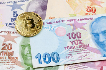 Close-up on a golden Bitcoin coin on top of a stack of Turkish lira banknotes.