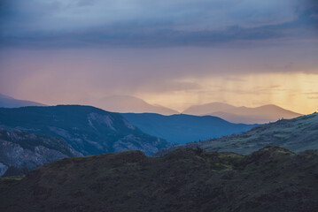 Atmospheric landscape with silhouettes of mountains with trees on background of vivid orange blue lilac dawn sky. Colorful nature scenery with sunset or sunrise of illuminating color. Sundown paysage
