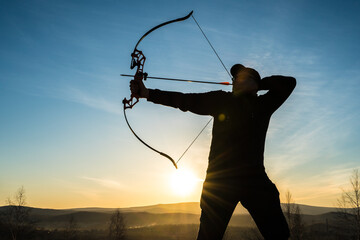 Silhouette of a hunter with a bow on a background of sunset. Hunting with arrows and a bow