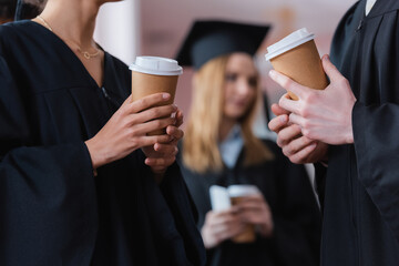 Cropped view of paper cups in hands of interracial graduates in university