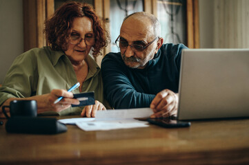 Senior couple using a laptop and a credit card at home