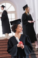 Cheerful african american student with diploma in university during graduation
