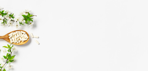 Collagen capsules for skin care and beauty in the wooden spoon on white background with blooming cherry branches. Health care concept. Long banner format.