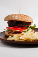 hamburger on a clay plate decorated with french fries and tomatoes on a white background.