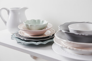 Piles of clean different shape size and color vintage style dishes plates in home kitchen shelf. Pastel color, white minimal background.
