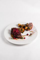 steak fillet mignon on a white plate decorated with cranberries and mushrooms champignons on a white background