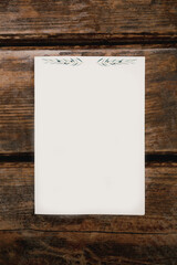 White vertical sheet with floral pattern at the top lies on a brown wooden table