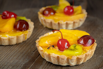 Three jelly tarts with fruits and cherry on brown wooden background