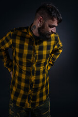 Attractive man with tattoos posing dressed in yellow and black checkered shirt on a black background