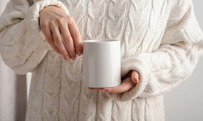 Female hands hold mock up white empty mug, cup for your design and logo close-up. Woman in beige...