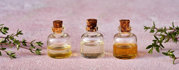 Panoramic banner of essential oil bottlesl with fresh thyme plant on pink background