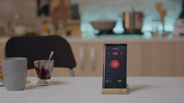 Smart home application on phone placed on kitchen desk in empty house automation system, turning on the light. Mobile with wireless lighting controlling, high tech to monitoring electricity effiency - Powered by Adobe