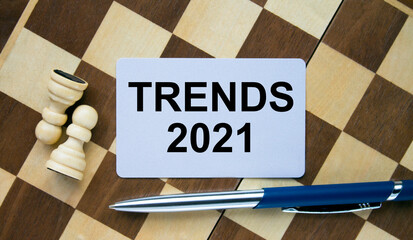 Business card with text Trends 2021 on a chess board with pen and eyeglasses