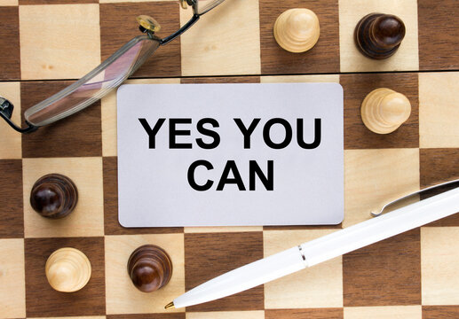 Business card with text Yes You Can on a chess board with pen and eyeglasses