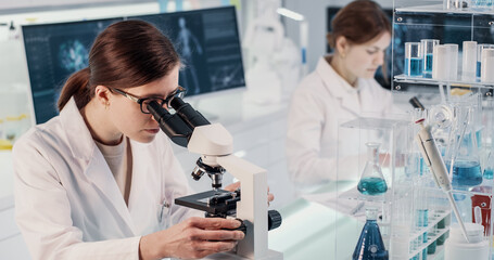 Female scientists working in laboratory. Studying medical samples with microscopes and using computers. Virus and human skeleton models on screens