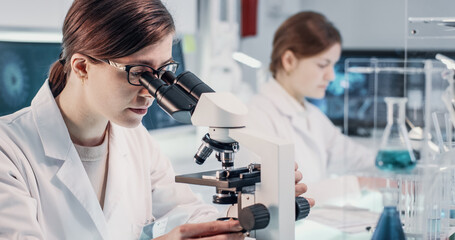 Female scientists working in laboratory. Studying medical samples with microscopes and using computers. Virus and human skeleton models on screens