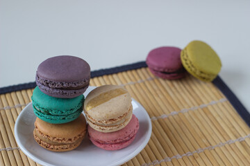Fototapeta na wymiar Plate full of colorful macaroons on light background on bamboo tablecloth.