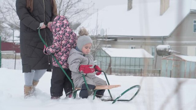 vacation, game, family concept - slo-mo authentic three happy preschool toddler kids siblings with young wonan mom sledding and play with snow. snowfall in cold season weather in winter yard outdoors